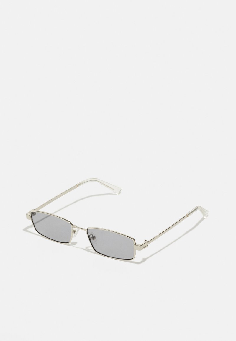 Lunettes de soleil avec des verres rectangulaires teintés gris ; monture en métal argenté fine ; branches transparentes ; design minimaliste sans motifs ni accents visibles.