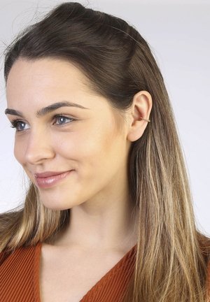 Gold hoop earring with a minimalist design, featuring a twisted texture and a small, intricate twist detail, seen on a model's ear.