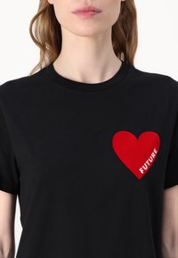 T-shirt en coton noir avec un grand graphisme en forme de cœur rouge et le mot "FUTURE" imprimé en blanc, col rond et manches courtes.