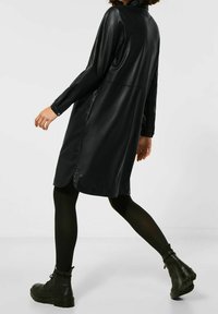 Svart skjortklänning i konstläder med lång ärm, sidofrvär, och en avslappnad siluett, kombinerad med svarta ankelstövlar.