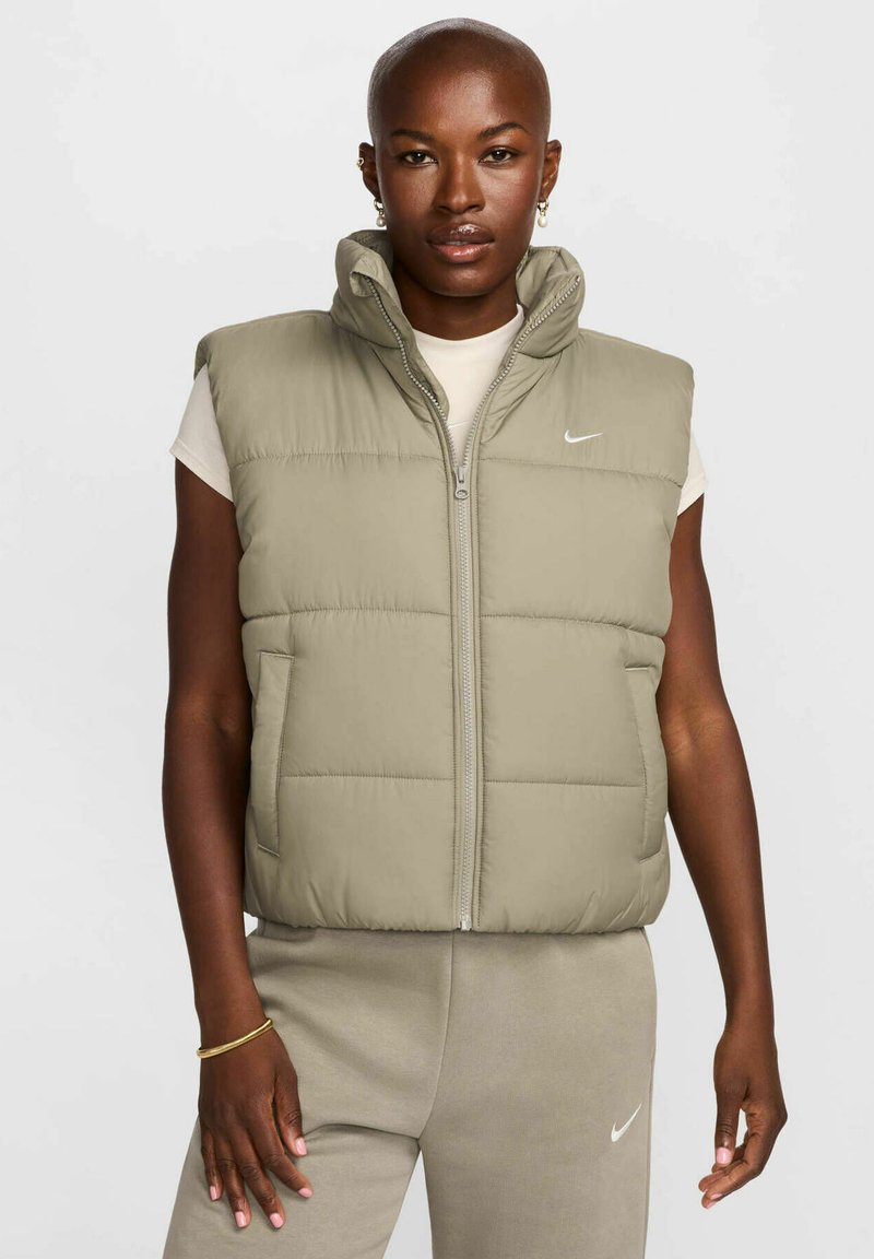 Gilet senza maniche imbottito di un verde oliva chiaro con alto collo, zip frontale e tasche laterali. Presenta il logo Nike sul petto.