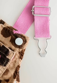 Rosa verstellbarer Gurt mit silbernem Metallverschluss, der an beigem und braunem Cord-Stoff mit einem silbernen Knopf befestigt ist.