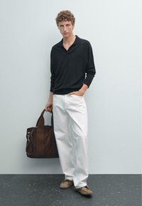 Černé polo tričko s dlouhým rukávem, bílé kalhoty, hnědé semišové boty a hnědá kožená taška. Jednoduchý design, volný střih a neutrální tóny.