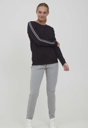 Svart hettegenser med hvite striper på ermene, kombinert med lysegrå joggebukser. Begge er laget av mykt, behagelig stoff med en avslappet passform.
