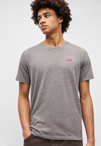 Camiseta gris de manga corta hecha de una mezcla de algodón, con cuello redondo y un pequeño logo rojo de Levi's en la parte izquierda del pecho.
