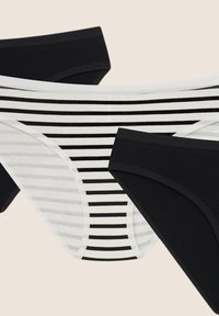 Trzy pary damskiej bielizny: jedna czarna, jedna gładka czarna, oraz jedna biała w czarne poziome paski.