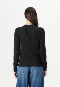 Pull en tricot noir avec un motif texturé, des poignets et un ourlet côtelés. Assorti à un jean en denim bleu ample. Vue arrière visible.