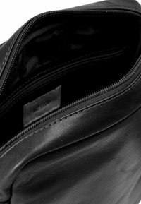 Borsa nera in pelle con texture liscia, dotata di apertura con cerniera e un interno semplice e senza ornamenti. Nessun hardware o particolari visibili.