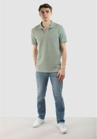 Ljusgrön kortärmad polo med en strukturerad ribbad design, tillsammans med blå jeans och vita sneakers. Enkel krage.