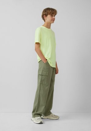 T-shirt jaune néon à manches courtes associé à un pantalon cargo vert olive avec des poches latérales. Des chaussures de sport décontractées complètent la tenue.