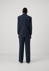 Jūrinė pinstripe kostiumas su pritaikytu švarku ir plačiomis kelnėmis. Yra notch tipo apykaklės ir mygtukų akcentai ant rankovių. Glotnus audinio tekstūra.