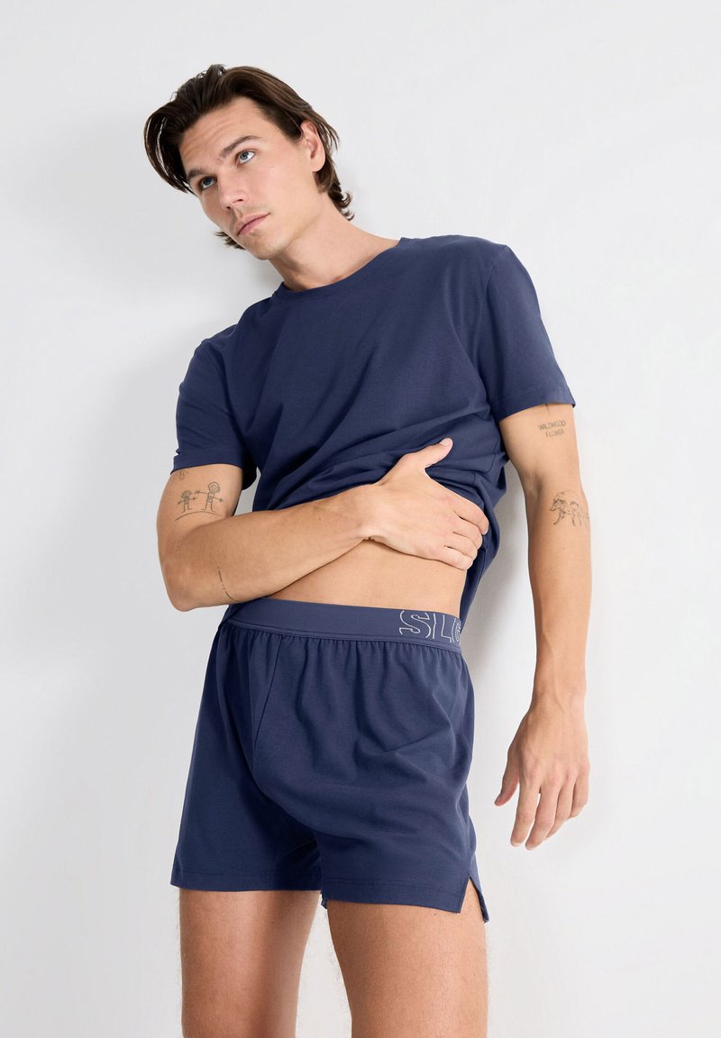 T-shirt en coton bleu marine à manches courtes et coupe décontractée, associé à un short assorti avec une taille logo et des fentes latérales.