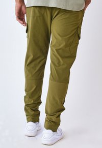 Pantalones cargo verde oliva con piernas ajustadas, tejido suave, bolsillos laterales y puños elásticos. Combinados con zapatillas blancas para crear contraste.