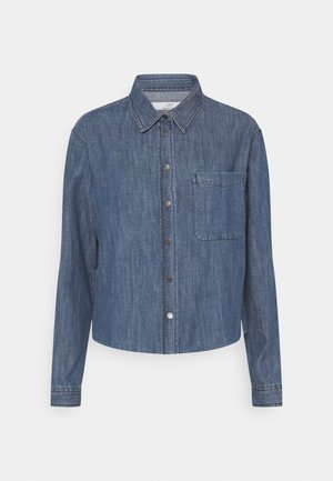 Veste en denim bleu au design court, avec fermeture à boutons, col pointu, manches longues et une poche poitrine. Texture lisse.