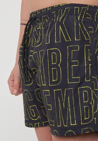 Costumi da bagno neri con lettering giallo audace, dotati di vita elasticizzata e lacci. Tessuto leggero con una superficie liscia.