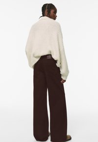 Maglione spesso lavorato a maglia abbinato a pantaloni a gamba larga marrone scuro con vita alta. Tessuto testurizzato e silhouette rilassata, con un lieve dettaglio del logo.