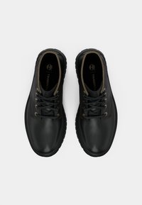 Scarpe in pelle nera con punta tonda, lacci piatti e suole in gomma. L'interno è foderato in marrone chiaro e presenta un logo sulla soletta.