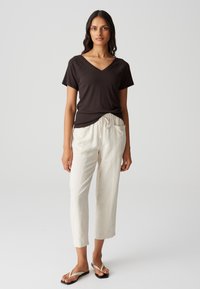 Schwarzes V-Ausschnitt-T-Shirt mit kurzen Ärmeln, kombiniert mit crèmefarbenen, leichten, knöchelfreien Hosen mit Kordelzug und Taschen.