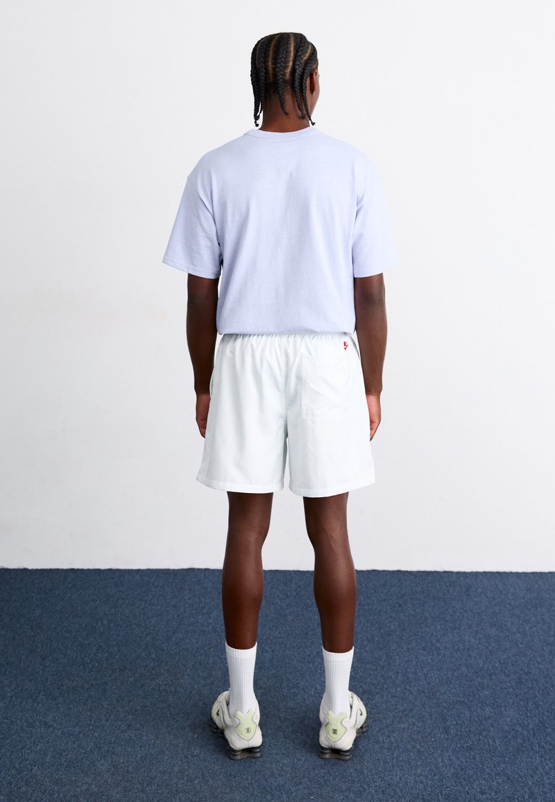 Helle lila Baumwoll-T-Shirt mit kurzen Ärmeln. Hellblaue Shorts mit elastischem Bund, Gesäßtasche, getragen mit weißen Socken und grauen Sneakers.