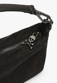 Sac en nylon noir avec une surface texturée, doté d'une fermeture éclair et d'un tirette de zip en forme de crâne et de tibias en argent, souligné par une sangle en cuir.