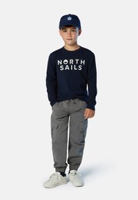 Camisa de manga larga navy con gráfico de "NORTH SAILS", pantalones cargo grises con puños elásticos, zapatillas blancas y gorra navy con logo.
