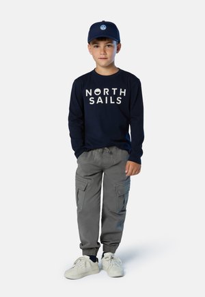 Camisa de manga larga navy con gráfico de "NORTH SAILS", pantalones cargo grises con puños elásticos, zapatillas blancas y gorra navy con logo.
