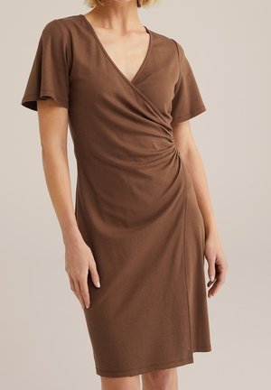 Bruine jurk tot op de knie met een V-hals, korte mouwen en een geplooid detail aan de zijkant. Gemaakt van zachte, rekbare stof voor een nauwsluitende pasvorm.