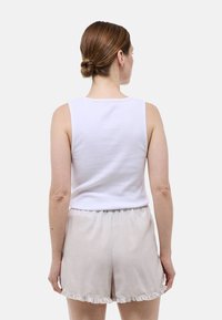 Un haut sans manches en coton blanc associé à un short rayé beige clair avec un ourlet volanté, vu de dos.