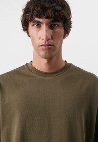 Oliven grøn bomulds t-shirt med rund halsudskæring og korte ærmer. Glat tekstur, minimalistisk design og ingen synlige mønstre eller accenter.