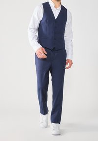 Námořnický oblek se štíhlou vestou, šesti knoflíky a kalhotami s plochým předním dílem. Nosí se s bílou košilí a bílými teniskami. Hladká textura tkaniny.