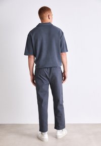 Mørkeblå, kortermet polo skjorte kombinert med matchende bukser. Buksene er litt smale med detalj på baklommen. Hvite sneakers brukes.