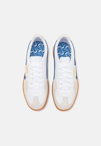 Vita sneakers med blå accenter och beige mockadetaljer. Har texturerade sulor, snören och mönstrade innersulor. Retrodesign.