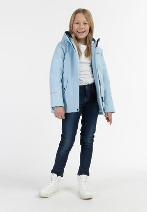 Lys blå, vandafvisende jakke med hætte, to sidelommer og lynlås. Bæres over en hvid skjorte og mørke jeans, med hvide sneakers.