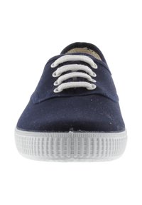 Sneaker in tela blu con suola in gomma bianca e lacci bianchi visti dal centro frontale.