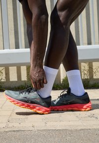 Scarpe da ginnastica atletiche con tomaia in rete grigia, dettagli neri e una suola con un vibrante gradiente dal rosa all'arancione. Presentano lacci e un design imbottito.