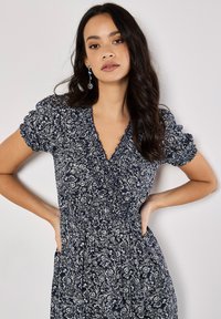 Marineblaues Blumenkleid mit kurzen Puffärmeln, V-Ausschnitt und geraffter Taille. Es zeichnet sich durch ein zartes weißes Blumenmuster aus.