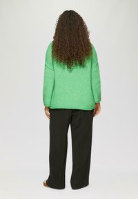 Grüner, gestrickter Pullover mit entspanntem Schnitt und überschnittenen Schultern, kombiniert mit schwarzen, weiten Hosen. Glatte Textur, schlichtes Design.
