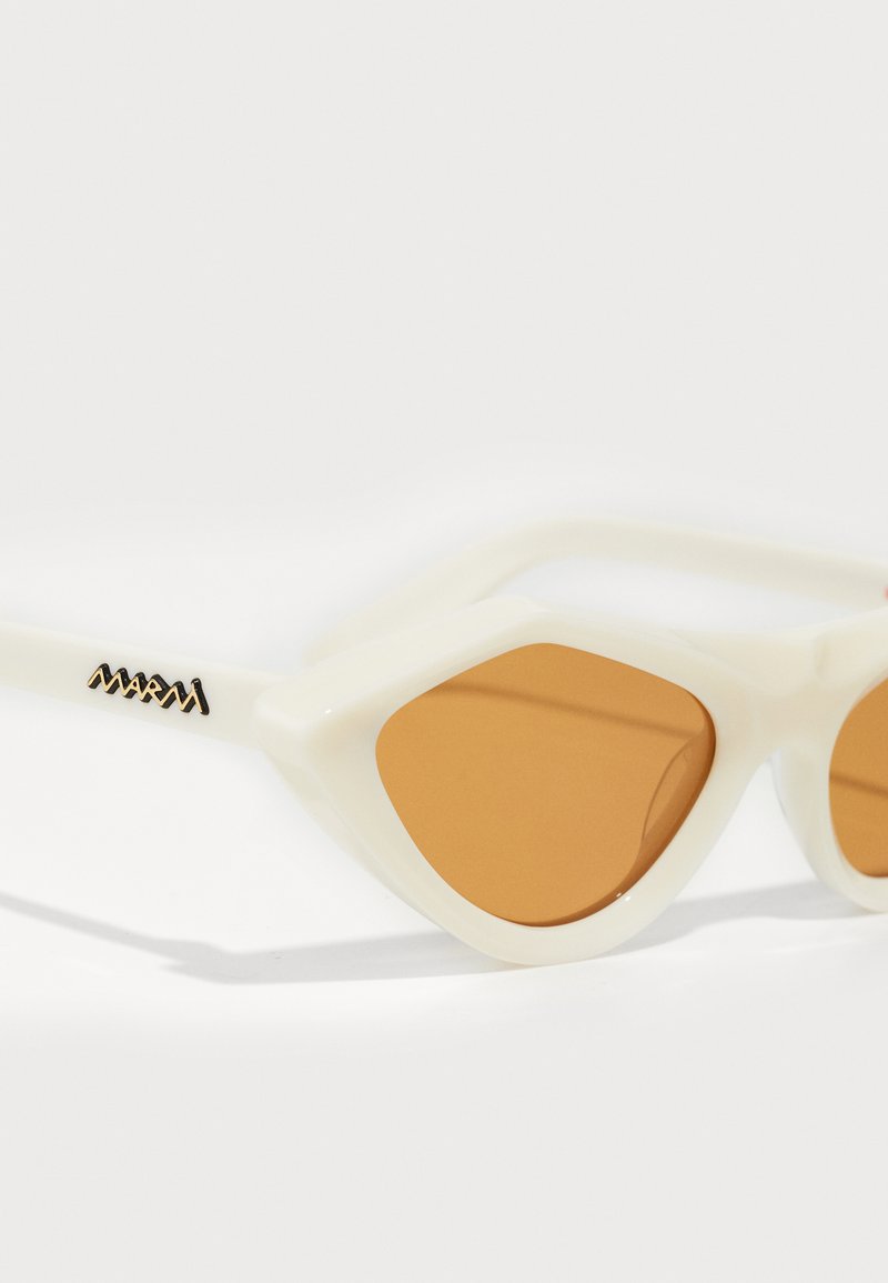 Occhiali da sole in plastica bianca con forma a occhio di gatto, dotati di lenti color brown. Accentuati con un logo nero sulla tempia.