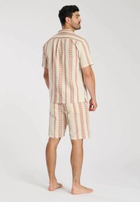 Set composto da camicia beige a maniche corte e pantaloni estivi, caratterizzato da un motivo geometrico in ruggine. Realizzato in un tessuto leggero con una vestibilità comoda.