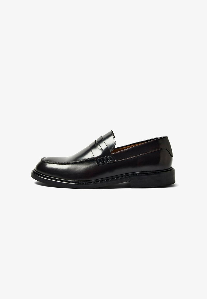 Μαύρο δερμάτινο παπούτσι τύπου penny loafer με χαμηλό τακούνι, στρογγυλεμένη μύτη και ραμμένες λεπτομέρειες κατά μήκος της επάνω και της σόλας.