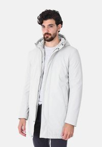 Giacca con cappuccio grigia chiara realizzata in tessuto morbido. Presenta una chiusura con zip, tasche laterali e una vestibilità leggermente sagomata.