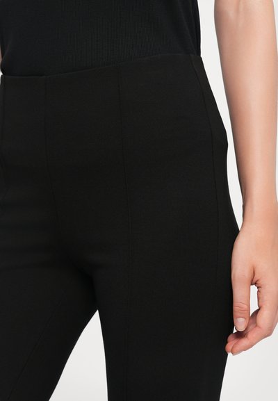 Black high-waisted pants made of soft, stretchy fabric; features smooth texture and clean lines, with a fitted silhouette and no visible hardware.
