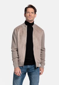 Lichtbeige bomberjack met een zachte suède voorkant en gebreide mouwen. Draag het over een zwarte turtleneck, gecombineerd met blauwe spijkerbroeken.