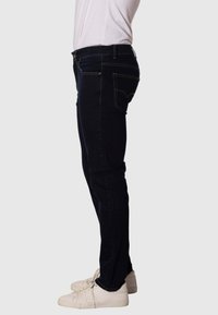 Jeans de mezclilla oscura con corte ajustado, con costuras amarillas y bolsillos traseros. Llevados con zapatillas blancas.