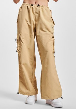 Pantalons cargo beiges avec taille élastique, poches latérales et ourlets à cordon de serrage. Fabriqués en matériau léger, avec une coupe décontractée.