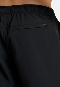 Black swim shorts made of lightweight fabric, featuring an elastic waistband, side pocket, and a small logo patch on the back.