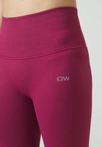 Ribbestrikkede leggings i magenta med høy midje. Har en liten grå logo på venstre side for merking. Glatt tekstur.