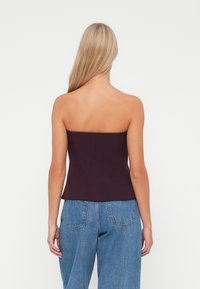 Burgundy strapless top with a fitted silhouette, featuring a smooth texture and clean lines. Paired with light blue wide-leg denim jeans.