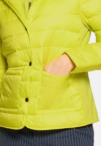 Kurtka puchowa w jaskrawym limonkowym kolorze o gładkiej fakturze, zapinana na zatrzaski, z widocznymi przeszyciami. Posiada dwie kieszenie oraz dopasowany kołnierz.