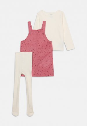 Une tenue pour enfant composée d’une robe chasuble rose à motifs, d’un haut crème à manches longues et d’un collant avec pieds crème.